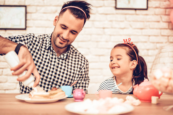 Father and Daughter on Sofa. Spend Time Together. Father's day. White Interior. Headband Hair on Head. Cakes on Plates. Bottle with Topping in Hand. Father Make Cupcake. Girl with Hairhoops. - Φωτογραφία, εικόνα