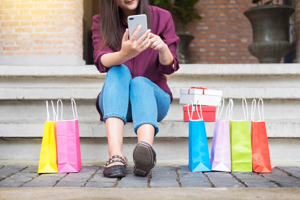 Mulher olhar para o telefone móvel com sacos de papel no shopping enquanto desfruta de um dia de compras
 - Foto, Imagem