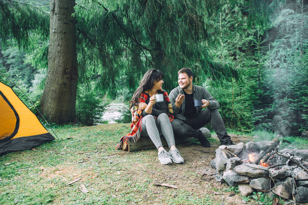 Çift oturma kamp ateşi yanında çay içmek ve hikayeler anlatmaya. çadır ve arka plan üzerinde suv. doğa ile Birliği - Fotoğraf, Görsel