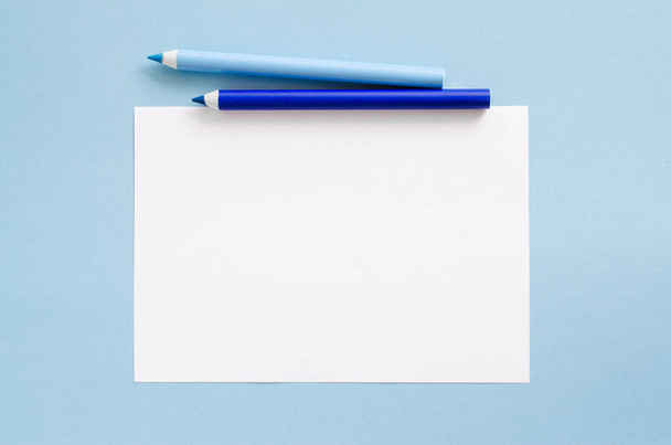 Λευκό κενό φύλλο χαρτιού και δύο μολύβια μπλε. Χώρο αντίγραφο μακέτα. Θέα από ψηλά, η έννοια της εκπαίδευσης. - Φωτογραφία, εικόνα