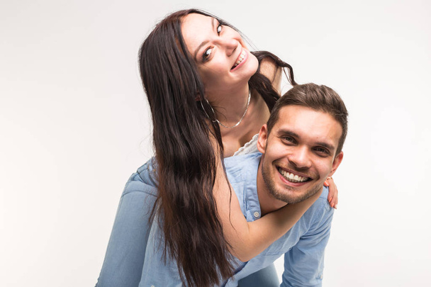 Young male carrying his girlfriend piggyback against a white background - Foto, Bild