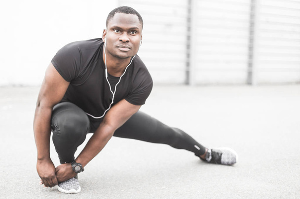 Young male jogger athlete training and doing workout outdoors in city. a black man resting after a workout and listening to music and watching a sports watch. free copyspace for text - Photo, Image