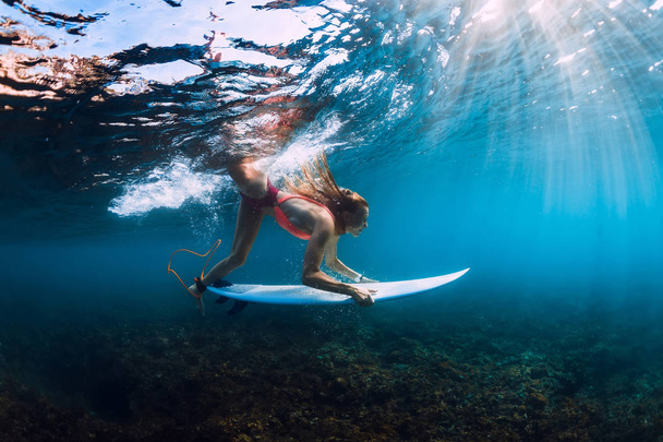 Surfer vrouw in bikini met surfboard duiken onder vat ocean wave - Foto, afbeelding