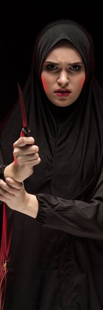 Muotokuva kaunis epätoivoinen peloissaan pelästynyt nuori musliminainen yllään musta hijabi pitämällä veitsi käsissään kuin suojelun käsite mustalla pohjalla
 - Valokuva, kuva