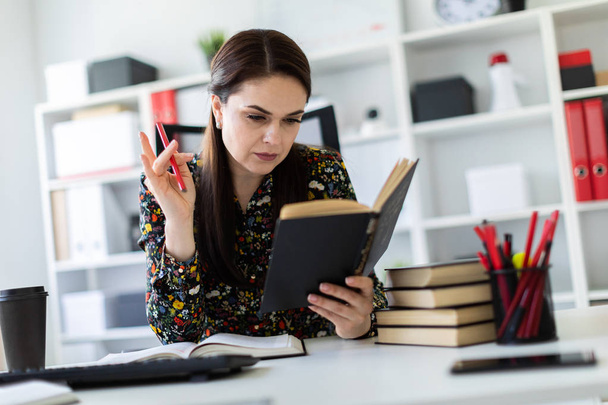 Uma jovem sentada no escritório na mesa do computador e trabalhando com um livro
. - Foto, Imagem