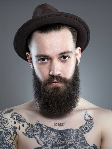 Красива бородата людина в капелюсі. Хіпстер хлопчик з татуюванням тіла
 - Фото, зображення