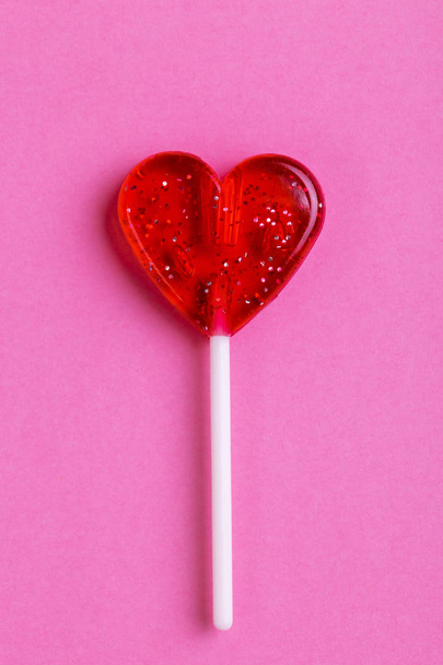 Red sweet tasty lollipop in shape of heart on bright pink background. St. Valentine's day. Copy space - Foto, Bild
