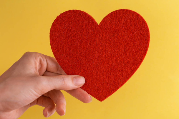 Red felt heart in woman's hand on bright yellow background. Copy space - Foto, Imagem