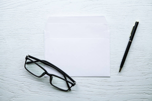  Envelope com óculos e caneta sobre fundo de madeira branca
. - Foto, Imagem