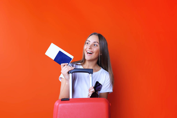 Young tourist girl in summer casual clothes, with sunglasses, red suitcase, passport isolated on red background. - Fotó, kép