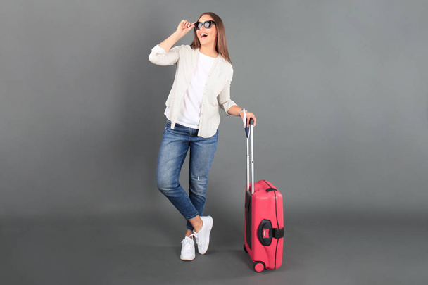 Young tourist girl in summer casual clothes, with sunglasses, red suitcase, passport, tickets isolated grey background. - Фото, зображення