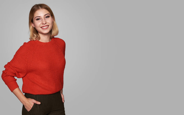 Pretty smiling woman is wearing red sweater isolated on grey studio background with copy space - 写真・画像