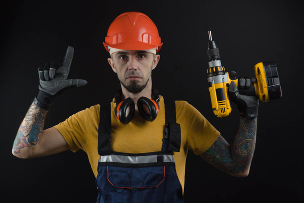a young man posing on a black background in a work uniform and a construction tool - Foto, Imagen