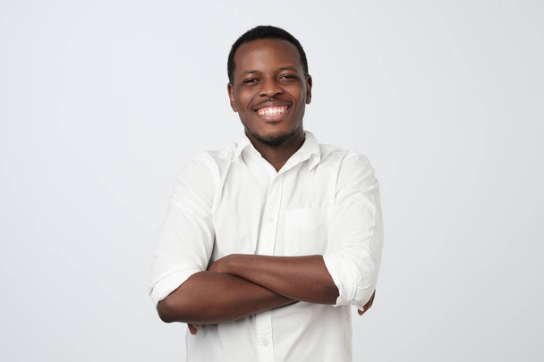 Retrato de hombre africano guapo feliz en camisa blanca cruzando las manos y mirar a la cámara. Emoción facial positiva
 - Foto, imagen
