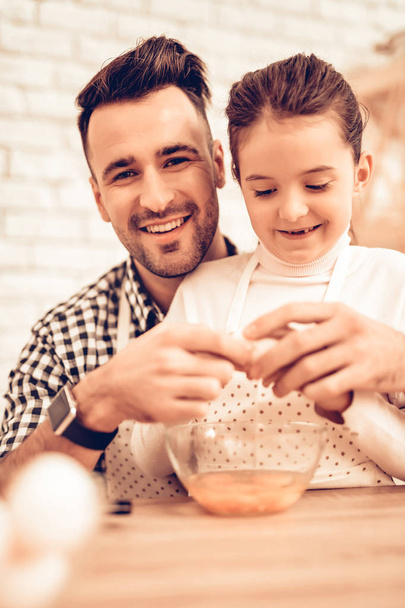 Cook Food at Home. Happy Family. Father's Day. Girl and Man Cook Food. Smiling Man and Child at Table. Spend Time Together. Knife in Hand. Tomatoes and Cucumber. Food on Table. Break Eggs into Bowl. - Fotografie, Obrázek