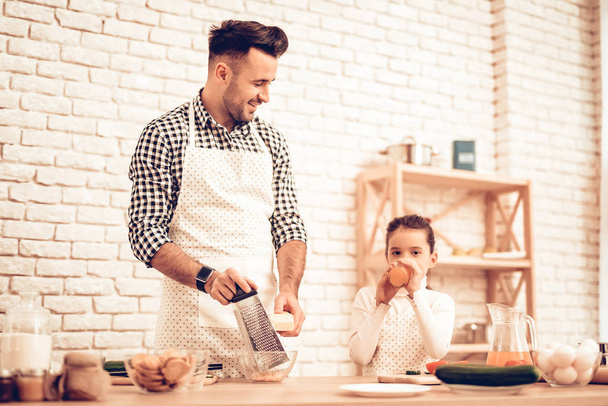 Cook Food at Home. Happy Family. Father's Day. Girl and Man Cook Food. Man and Child at Table. Spend Time Together. Grate Cheese. Grater in Hand. Tomatoes and Cucumber. Drink Juice. Rub Grated. - Fotoğraf, Görsel