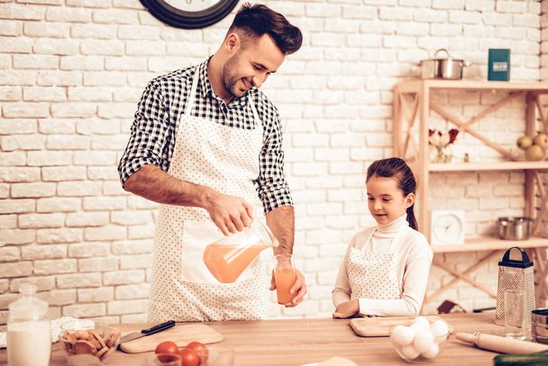 Cook Food at Home. Father Feeds Daughter. Pour Juice in Glass. Happy Family. Father's Day. Girl and Man Cook Food. Man and Child at Table. Spend Time Together. Dad with Carafe in Hand. Family at Home. - Φωτογραφία, εικόνα