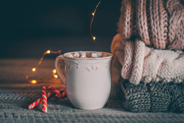 Montón de suéteres de punto acogedor y taza de café o chocolate caliente con malvavisco sobre fondo de madera. Concepto otoño-invierno. Magia, acogedor y el tiempo de ánimo
 - Foto, imagen