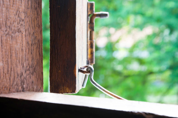 STEEL-HOOK HOLDING OPENING WINDOW OF VINTAGE WOODEN HOUSE IN MORNING TIME , BLURRY GREEN TREE OUTSIDE BACKGROUND - Photo, Image