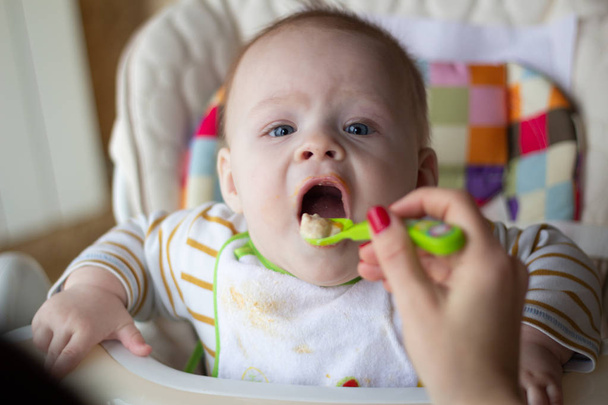 Az első etetése a baba a kanalat. Anya eszik baba homogenizált apróra vágott étel egy kanállal. gyermekfelügyelet - Fotó, kép