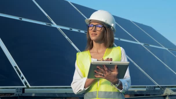 Smiling lady expert is standing near a solar battery with a tablet - Filmati, video