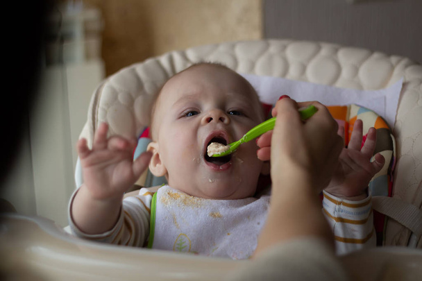 La primera alimentación del bebé de la cuchara. Mamá alimenta al bebé con una cuchara de comida picada homogeneizada. cuidado de niños
 - Foto, imagen
