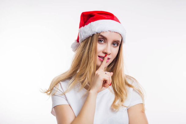 Smiling happy girl says Shh, secret and puts finger on lips on white background. Christmas, new year and celebration concept - Фото, изображение