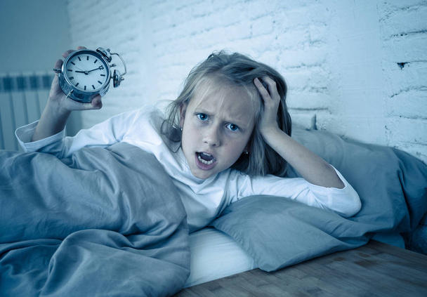 Sweet sleepless little girl stressed sad and angry in bed looking at alarm clock having to wake up but feeling sleepless in Troubles staying asleep Sleep disorder and Children Insomnia concept. - Foto, Bild