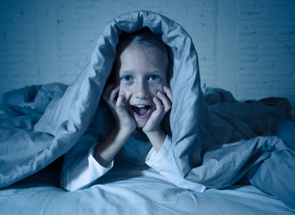 Cute asleep girl screaming and crying after frightening or upsetting dream covering herself with blanket in bed at night in mood dramatic lighting in Sleep terrors Nightmares and Sleeping disorders. - Фото, изображение