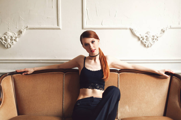 Sexually attractive girl sitting and posing on sofa in sexy lace top and black jeans with naked stomach - Φωτογραφία, εικόνα