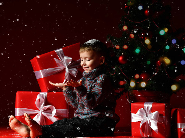 αγοράκι την παραμονή της Πρωτοχρονιάς και των Χριστουγέννων είναι κάθεται κάτω από το δέντρο - Φωτογραφία, εικόνα