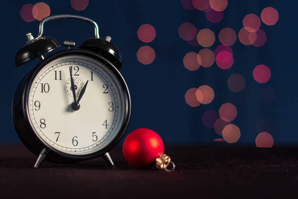 Der Wecker zeigt zwei Minuten vor zwölf auf einem Hintergrund aus Weihnachtslichtern. das Konzept eines neuen Jahres. - Foto, Bild