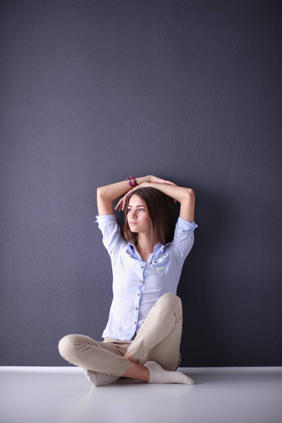Portrait of a casual happy woman sitting on the floor on gray background - Foto, Imagem