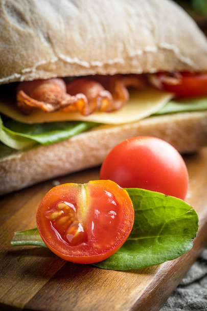 Ciabatta sandwich with arugula salad, bacon and yellow cheese on wooden board. - Фото, зображення