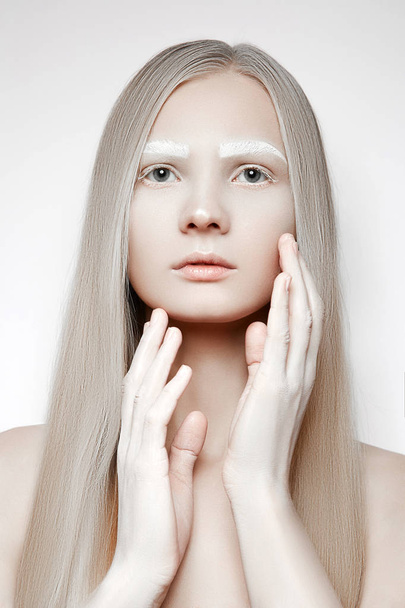 Portrait of a young girl with blond hair. White makeup on the eyebrows. Girl touches face with her hands - Photo, Image