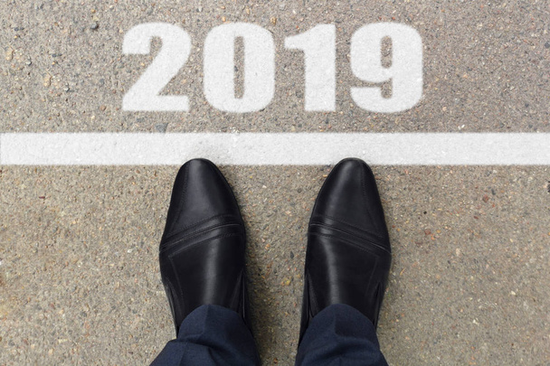 Man feet in black leather shoes standing before text 2019 painted on asphalt, top view - Photo, Image