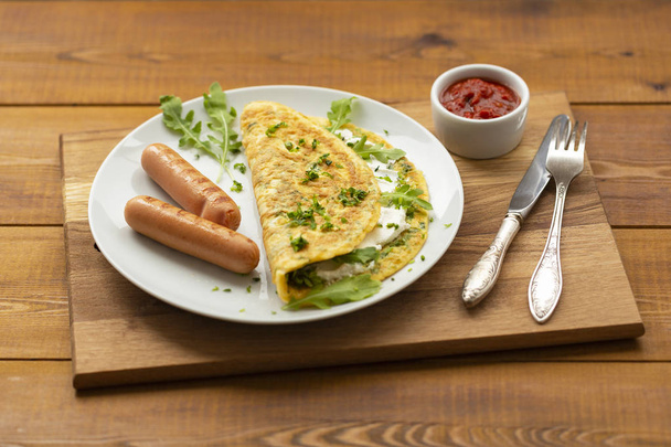 Omelette with herbs, soft cheese, grilled sausages and tomato sauce. Delicious breakfast - Fotó, kép