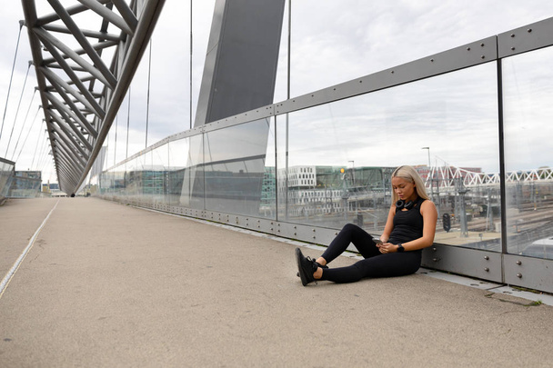 Běžec sedí na mostě po cvičení a pomocí chytrého telefonu - Fotografie, Obrázek