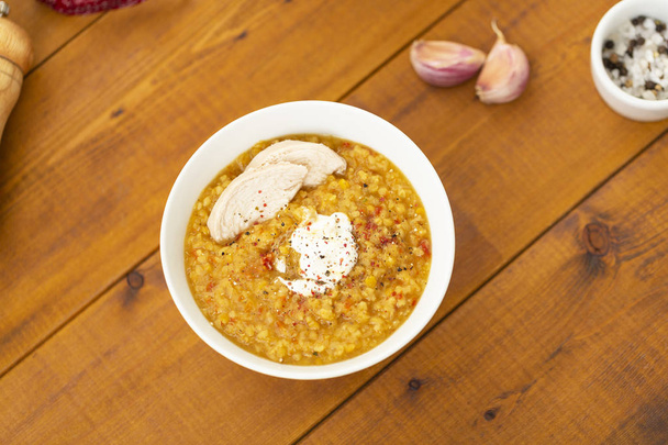 Turkish lentil bulgur soup sprinkled with pepper in a white bowl on a wooden background - Valokuva, kuva