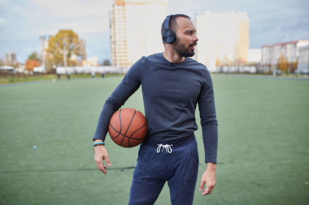 atleta con una pelota de baloncesto en el estadio. Joven con auriculares sosteniendo una pelota de baloncesto
 - Foto, Imagen