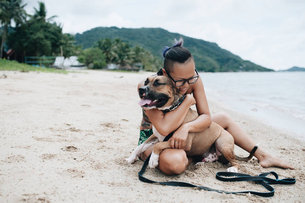 Wesoły dość młoda kobieta w eyeglases siedzi i przytulanie jej pies na plaży - Zdjęcie, obraz