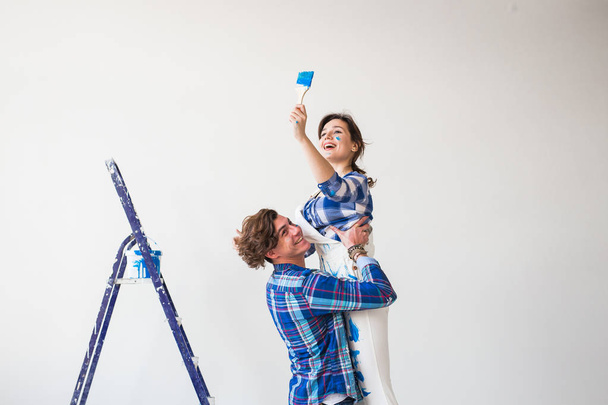 Ремонт, ремонт и семейная концепция - Молодой человек держит молодую женщину на руках во время ремонта в квартире
. - Фото, изображение