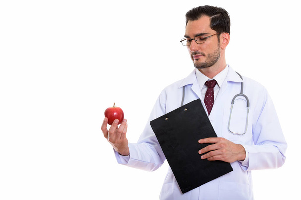 Студійний знімок молодого красивого лікаря, який тримає кишеню і дивиться на червоне яблуко
 - Фото, зображення