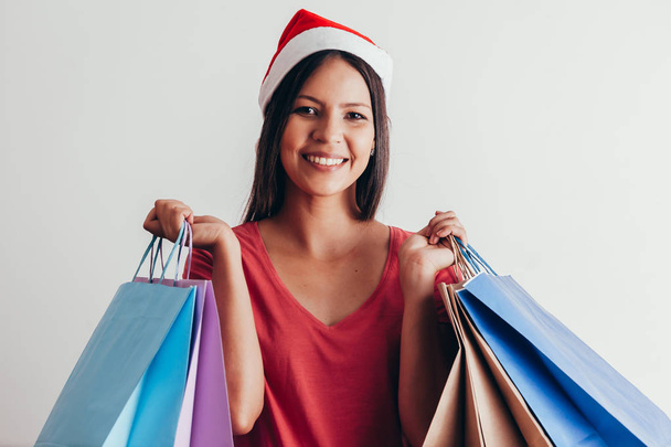 Young woman in santa hat with shopping bags on white background - Fotoğraf, Görsel