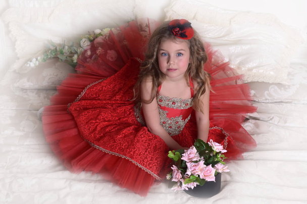 portrait of a little girl princess in a red dress and a hat sits on the sofa with a box of roses - Fotoğraf, Görsel