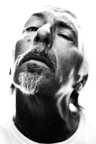 Hoher Kontrast, Hintergrundbeleuchtung, Schwarz-Weiß-Porträt eines Mannes mit nach hinten geneigtem Kopf, der gequält wirkt, flache Schärfentiefe mit 100% Korn - Foto, Bild