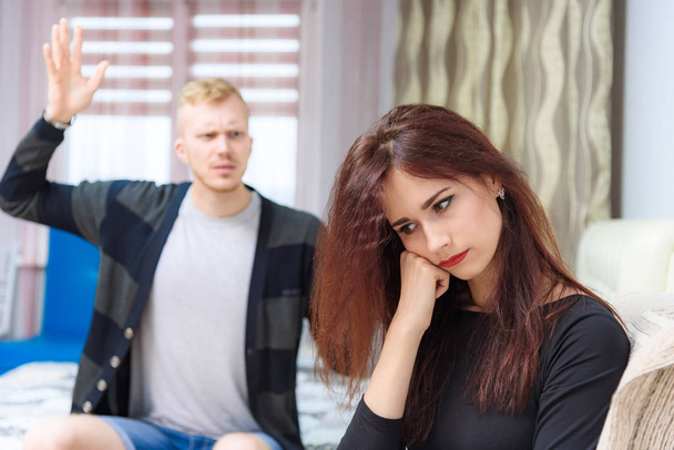 The concept of family conflict, family problems, family relationships of young disgruntled husband and wife in a room on the sofa. They sit across from each other and look displeased. - Valokuva, kuva