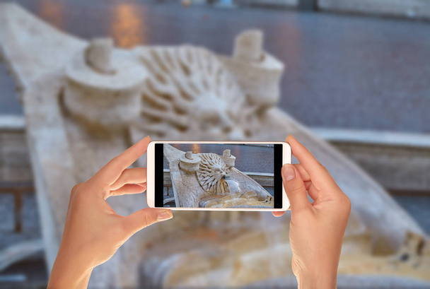 Ένας τουρίστας παίρνει μια φωτογραφία του λεπτομέρεια από την Κρήνη της Πιάτσα του σπάνια κοντά στα Ισπανικά Σκαλιά στη Ρώμη σε ένα κινητό τηλέφωνο - Φωτογραφία, εικόνα