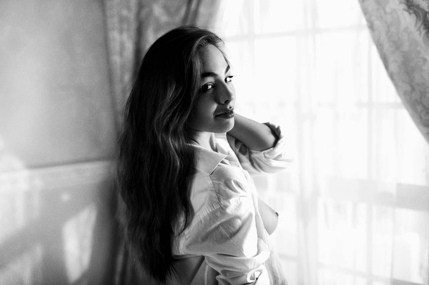 Beautiful girl with long hairs in unbuttoned man's shirt teasing - 写真・画像