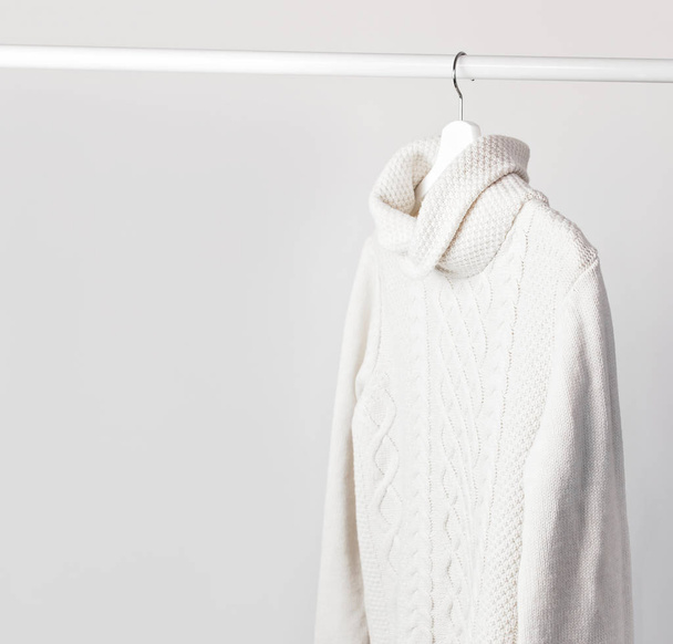 White knitted wool sweater on a white wooden hanger against the background of the light wall. Autumn and winter clothes. Store concept, sale design. Place for text. - Valokuva, kuva
